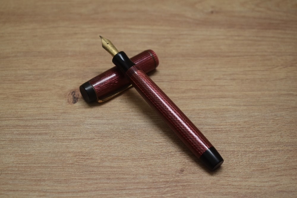 A Parker Duofold Senior Streamlined button fill fountain pen in black and red herringbone with one: A Parker Duofold Senior Streamlined button fill fountain pen in black and red herringbone with one cap band having Parker Duofold 14k Pen N nib. Condition Report - Barrel imprint slightly worn, no cra