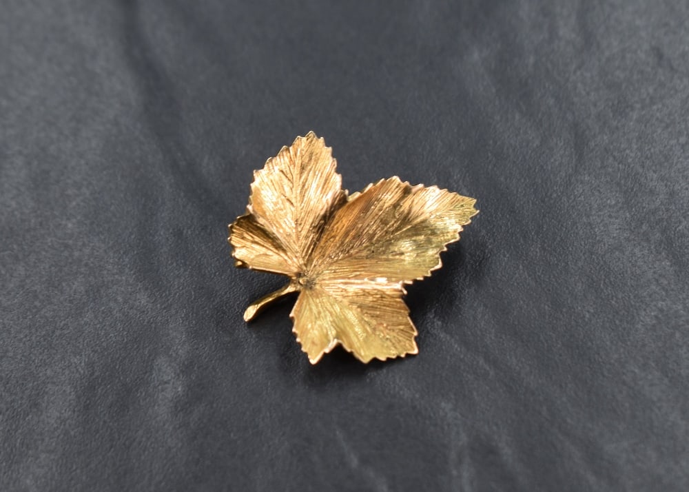 A 9ct gold leaf brooch, the maple motif leaf having a textured surface, with loop for safety chain: A 9ct gold leaf brooch, the maple motif leaf having a textured surface, with loop for safety chain to reverse, 5.2g