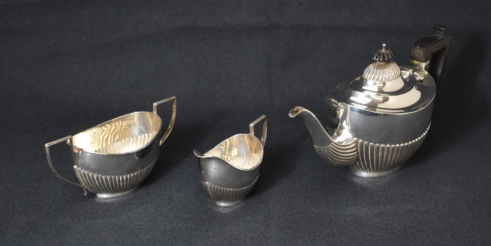 A late Victorian silver three piece tea set, comprising a tea pot, sugar and milk each of oval: A late Victorian silver three piece tea set, comprising a tea pot, sugar and milk each of oval half-gadrooned form with angular handles, marks for Birmingham 1900, 1901, maker Joseph Gloster, 737g gro