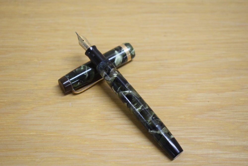 A Parker Duofold Standard button fill fountain pen in green and black marble with broad gold cap: A Parker Duofold Standard button fill fountain pen in green and black marble with broad gold cap band having Parker Duofold 14K Pen N nib.