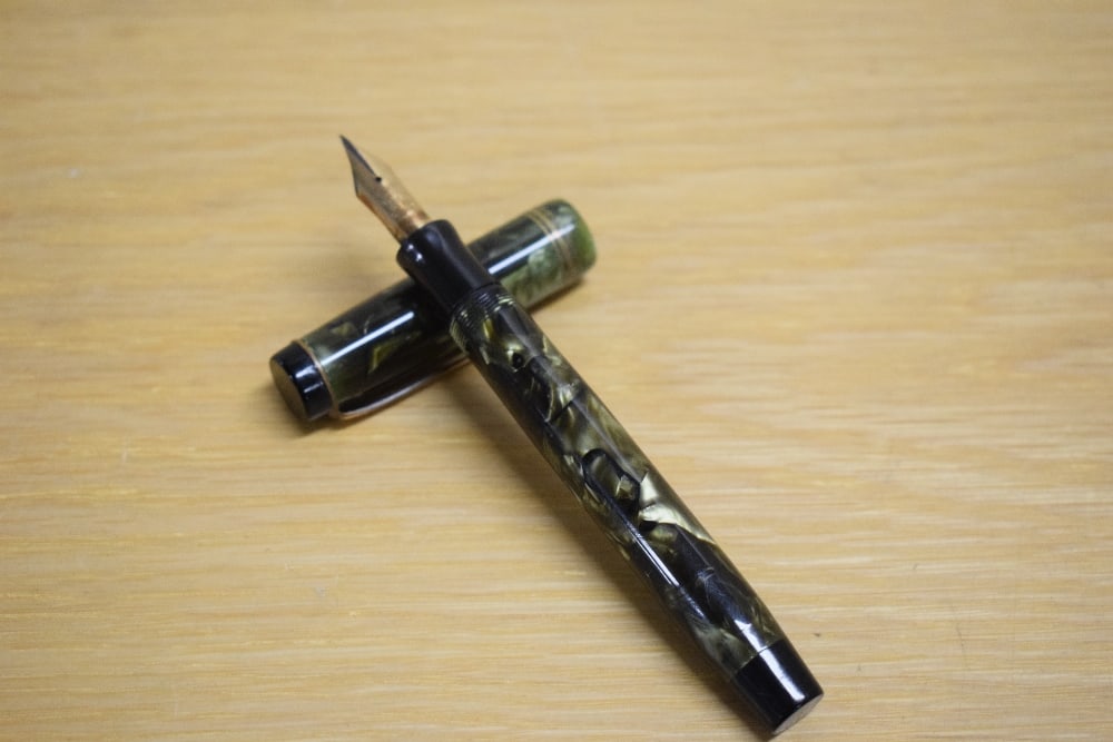 A Parker Duofold Deluxe Special button fill fountain pen in green and black marble with two narrow: A Parker Duofold Deluxe Special button fill fountain pen in green and black marble with two narrow and one broad cap bands having Parker Duofold 14k Pen Canada 35 nib.