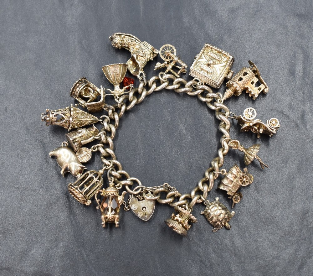 A silver charm bracelet having padlock clasp and sixteen charms including church, holy bible, boot: A silver charm bracelet having padlock clasp and sixteen charms including church, holy bible, boot etc, approx 101g Condition report: approximately 18cm in length 