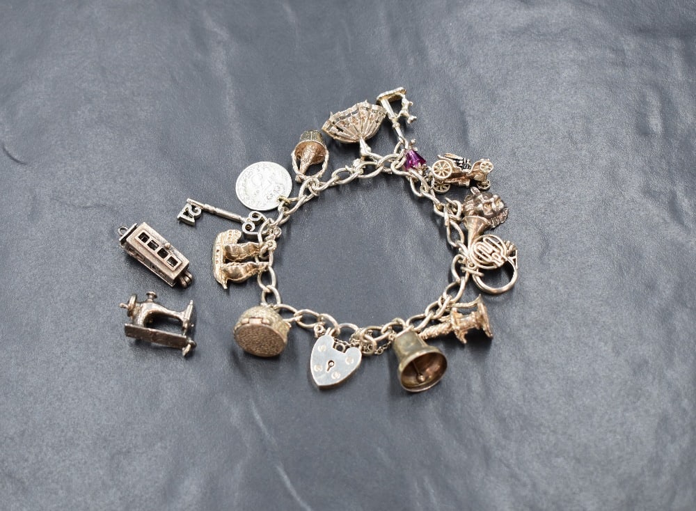 A silver curb link charm bracelet, having a heart padlock and thirteen white metal charms (1 of 1)