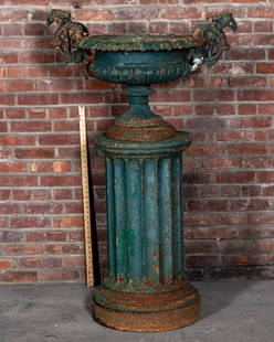 Cast Iron Victorian Pierced Two Arm Urn on Fluted Pedestal in a Green Painted Distressed Finish: Cast iron Victorian two arm Neoclassical style decorative garden urn on a fluted Doric column pedestal in a distressed, green painted finish. The urn features pierced, scrolled foliage on the arms