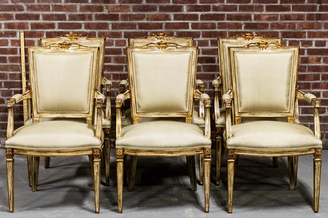 Set of Six Giltwood Open Armchairs with Silk Upholstery: Set of six open armchairs upholstered in silk with metal nail head trim. The rectangular seatbacks feature a carved cupid's bow shaped top rail with a central urn motif flanked by laurel swags. The ar
