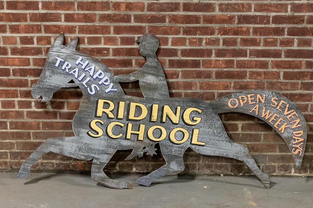 Horse Riding Trade Sign from the State of Maryland in the United States: Hanging trade sign for Happy Trails Riding School based in western Maryland. The sign is constructed in the silhouette of a galloping horse with spur booted rider. The original painted calligraphy rea