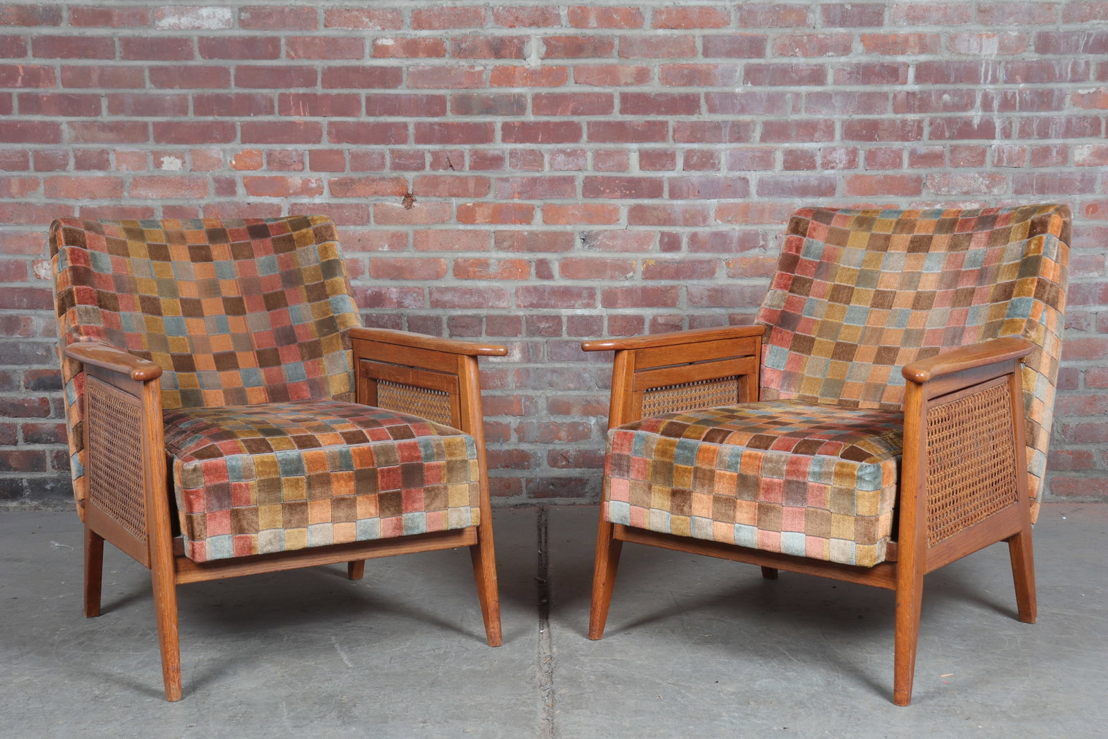 Pair of Midcentury Lounge Chairs: Pair of midcentury arm chairs with checkerboard upholstery, flip down rattan side-shelves, and tapered splayed legs. Seat height 16"