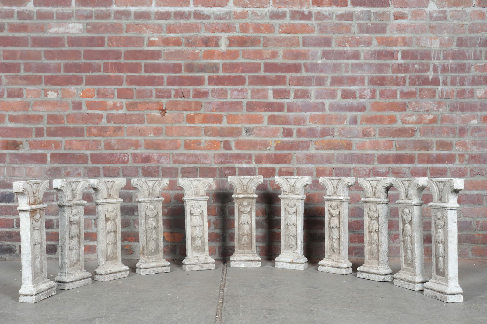 Group of Eleven Concrete Balusters: A set of eleven matching concrete balusters with floral festoon motifs.
