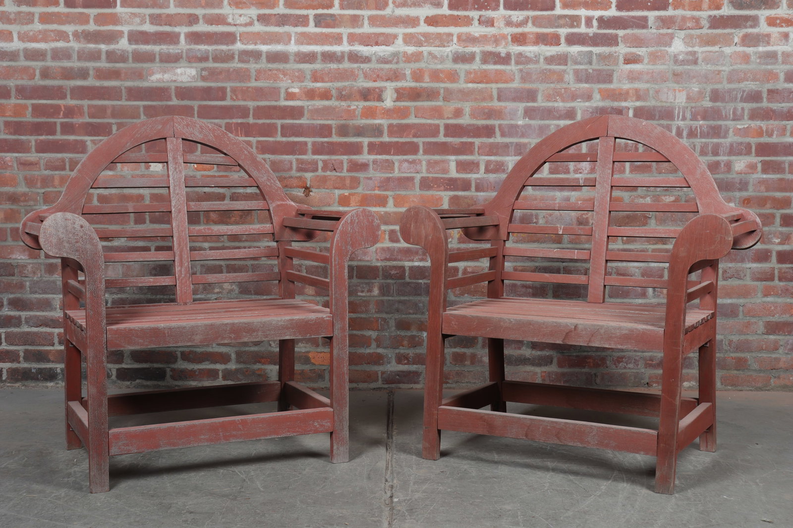 Pair of Teak Garden Chairs: Pair of faded red patina teak garden arm chairs with stretchers, rounded backs, and rounded arms. Repaired with some evidence of birds having enjoyed these chairs. Seat height 17.5"