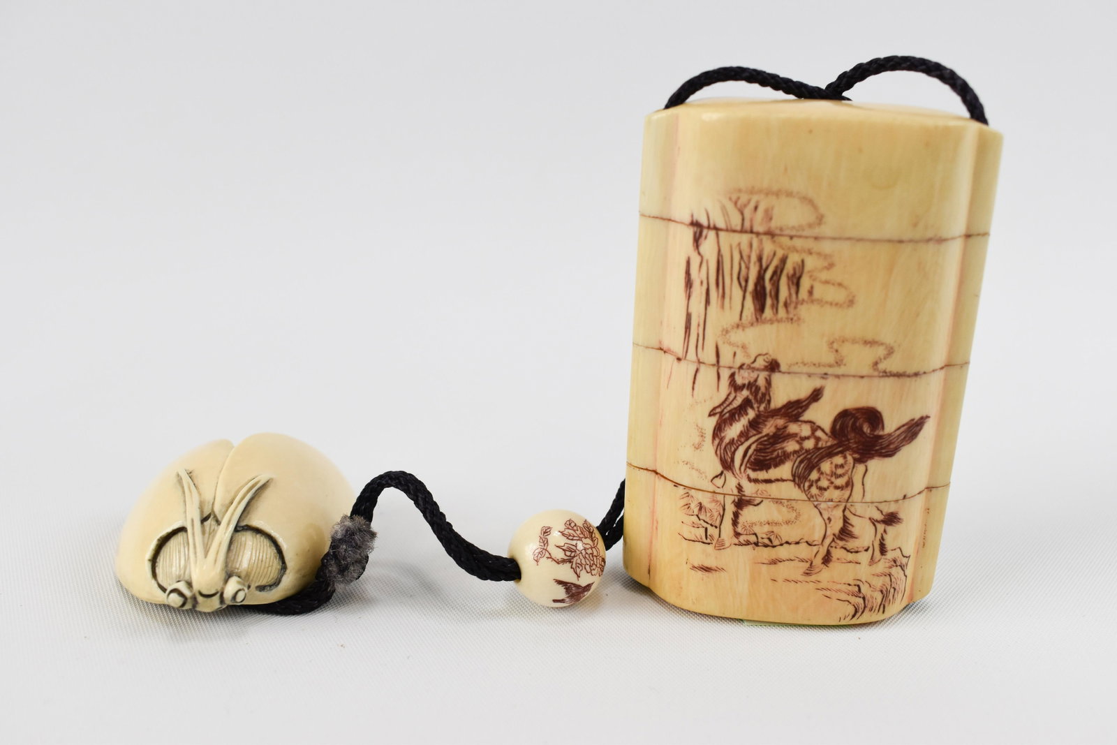 Ivory Inro with Ojime and Netsuke: Japanese, First Half 20th Century The inro with three cases, incised with a landscape on one side and a kirin on the other, picked out in brown pigment: with a simple ivory bead ojime and an ivory lad