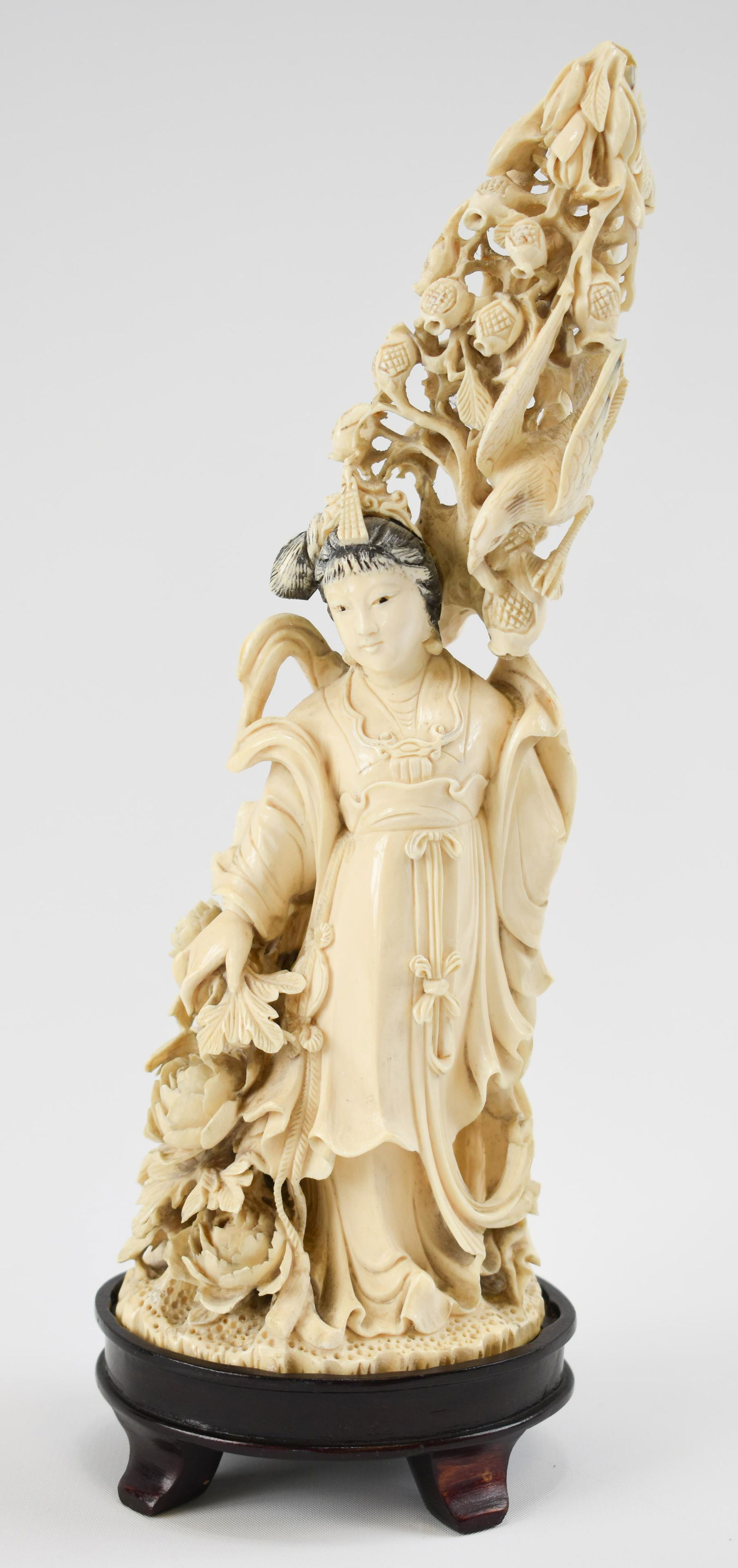 Carved Ivory Figure of a Meiren ("Beauty"): Chinese, First Half 20th Century The young girl wearing a belted skirt over a long robe, holding oversize peony in one hand and a pomegranate branch in the other; a wood stand. Height: 9 1/2"