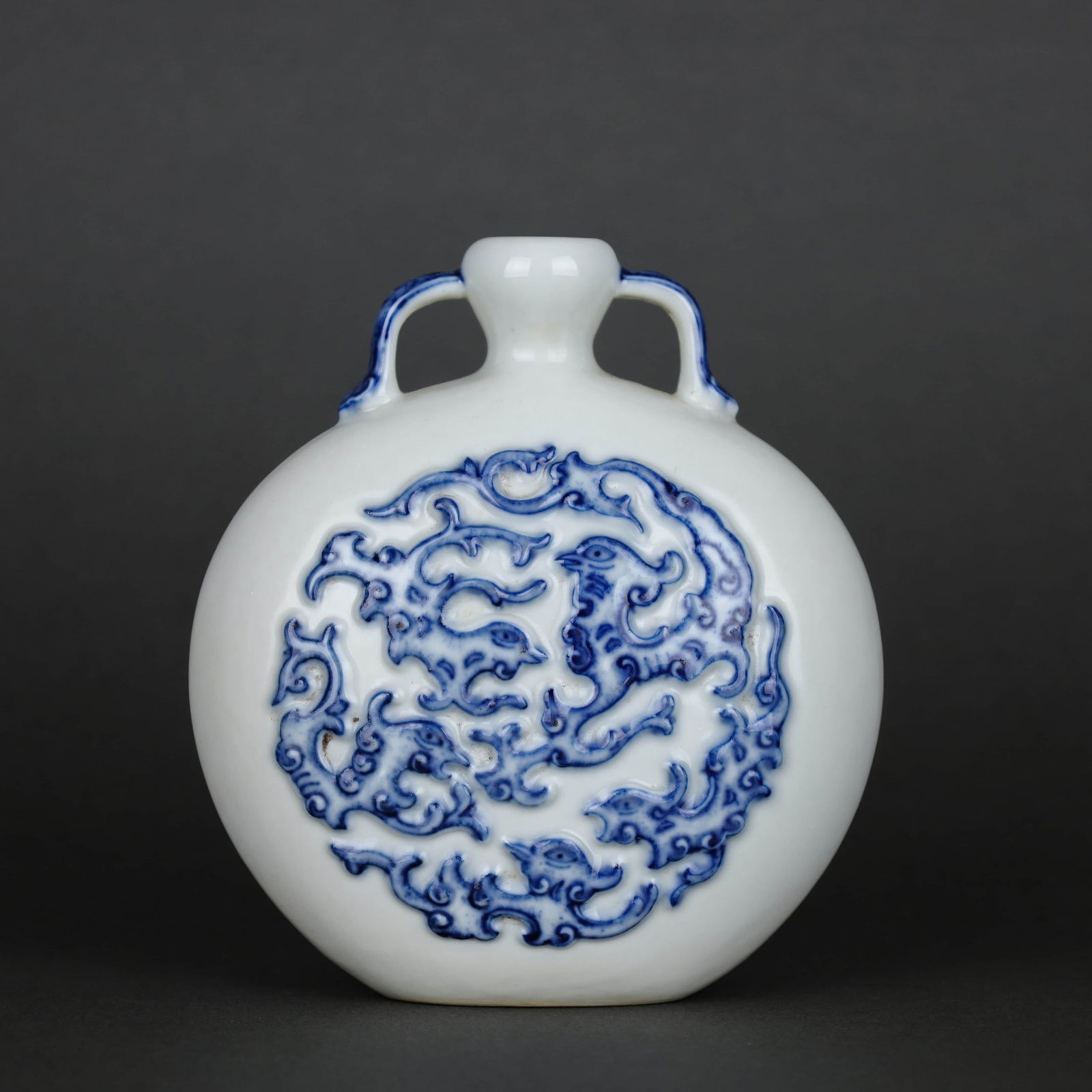 A WHITE-GLAZED BLUE AND WHITE CARVED 'DRAGON' MOONFLASK: A WHITE-GLAZED BLUE AND WHITE CARVED 'DRAGON' MOONFLASK Dimensions: Height: 13 cm (5.12 in.), Diameter: 11.8 cm (4.65 in.). All measurements are approximate.