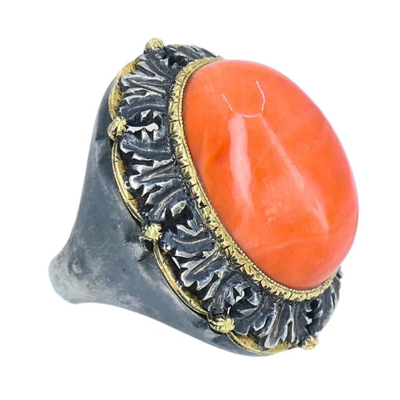 CORAL CABOCHON RING: CORAL CABOCHON RING Description: A ring centered by an oval coral-colored cabochon in a dark-toned and yellow metal mount with decorative surround. The images show the ring face and profile.