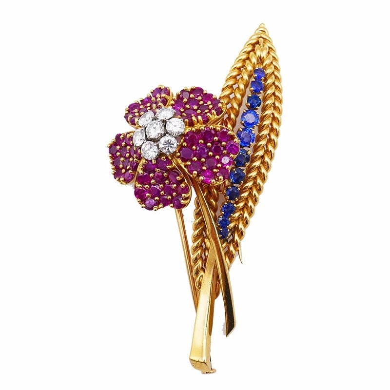 RUBY, SAPPHIRE AND DIAMOND FLORAL BROOCH: RUBY, SAPPHIRE AND DIAMOND FLORAL BROOCH Description: A yellow metal floral brooch set with red, blue and white stones in a ribbon-like arrangement. The images show the front, reverse and side profile