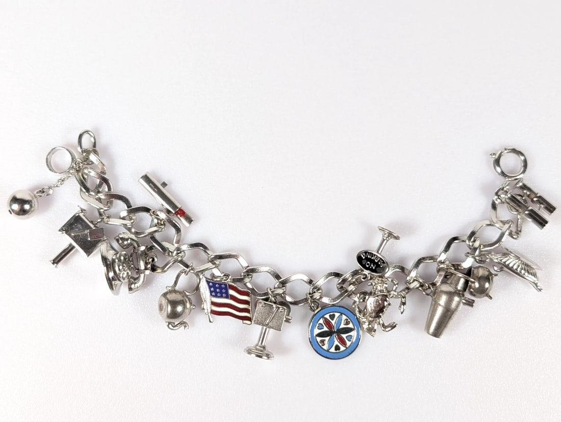 SILVER CHARM BRACELET: SILVER CHARM BRACELET Description: A silver charm bracelet with assorted hanging charms, including travel, symbolic and decorative forms. The image records the bracelet laid flat for catalogue review.
