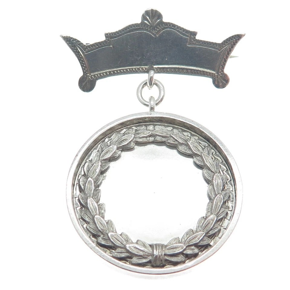 VINTAGE SILVER-TONE WREATH-FORM MEDAL OR BADGE: VINTAGE SILVER-TONE WREATH-FORM MEDAL OR BADGE Description: The piece is designed with a shaped and slightly arched upper suspension element above a circular pendant formed as an openwork wreath. The