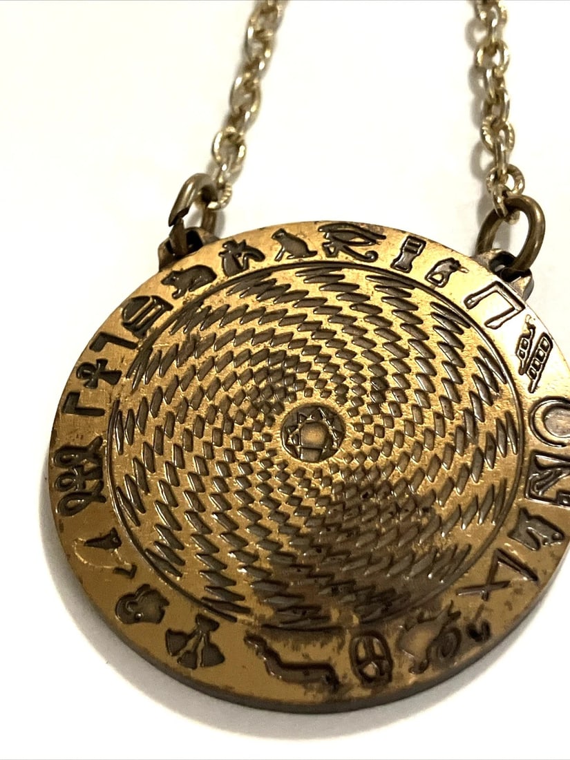 EGYPTIAN REVIVAL GOLD-TONE SYMBOLIC AMULET PENDANT WITH HIEROGLYPHIC DECORATION (20TH CENTURY): EGYPTIAN REVIVAL GOLD-TONE SYMBOLIC AMULET PENDANT WITH HIEROGLYPHIC DECORATION (20TH CENTURY) Description: A striking gold-tone pendant of circular form, decorated with a richly detailed engraved