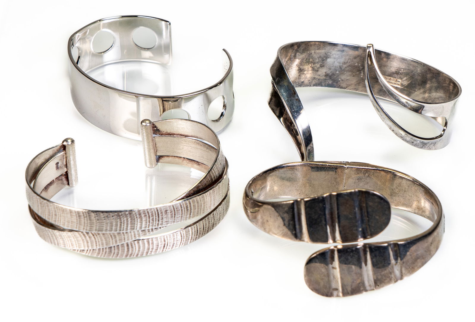 Four (4) Sterling Silver Cuff Bracelets: Four (4) sterling silver cuff bracelets of different shapes and designs, including: One simple cuff pierced with 6 circular holes, marked "Kenwood, Sterling" (Approximately 7 in., inner circumference)