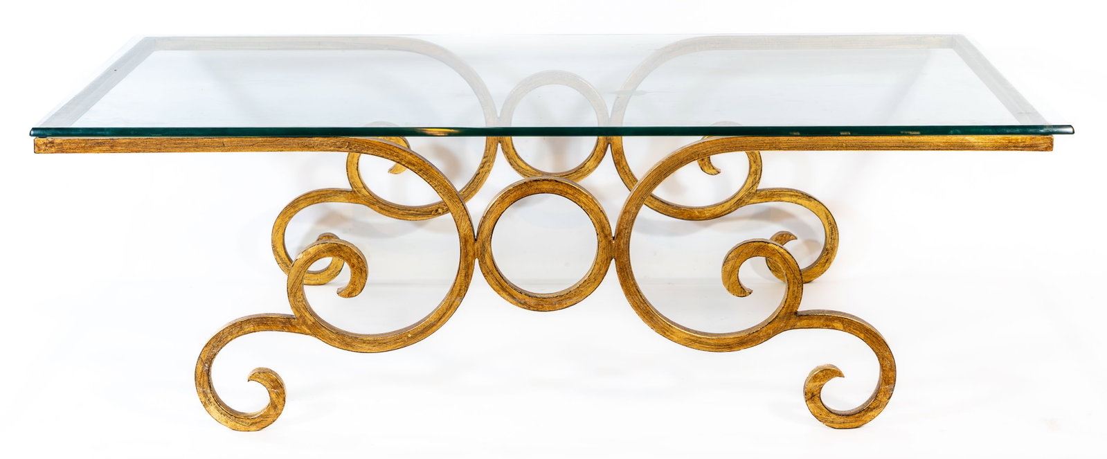Hollywood Regency Scrolled Gilt Iron Coffee Table: Hollywood Regency style coffee table with glass top on scrolling gilt wrought iron base. Dimensions: 16 in. high x 52.5 in. wide x 30 in. deep. Condition: No notable issues.