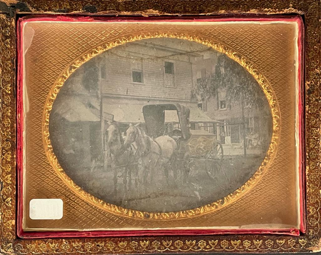 [DAGUERREOTYPE] OUTDOOR SCENE WITH FUNERAL WAGON: Anonymous [Outdoor scene with horses and buggy, in front of a barber shop appears to have a coffin with gold decoration] Sixth plate daguerreotype in wall hanging frame n/d Additional images and detai