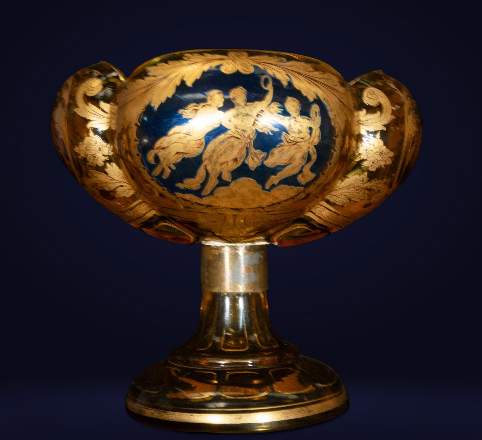 Italian glass centerpiece with allegorical scenes. Venetian School. 19th century: Blown and enameled glass with gold decoration. This intense orange Italian glass piece features a bulbous shape, raised on a truncated cone-shaped shaft with a circular base. The belly features a dyna