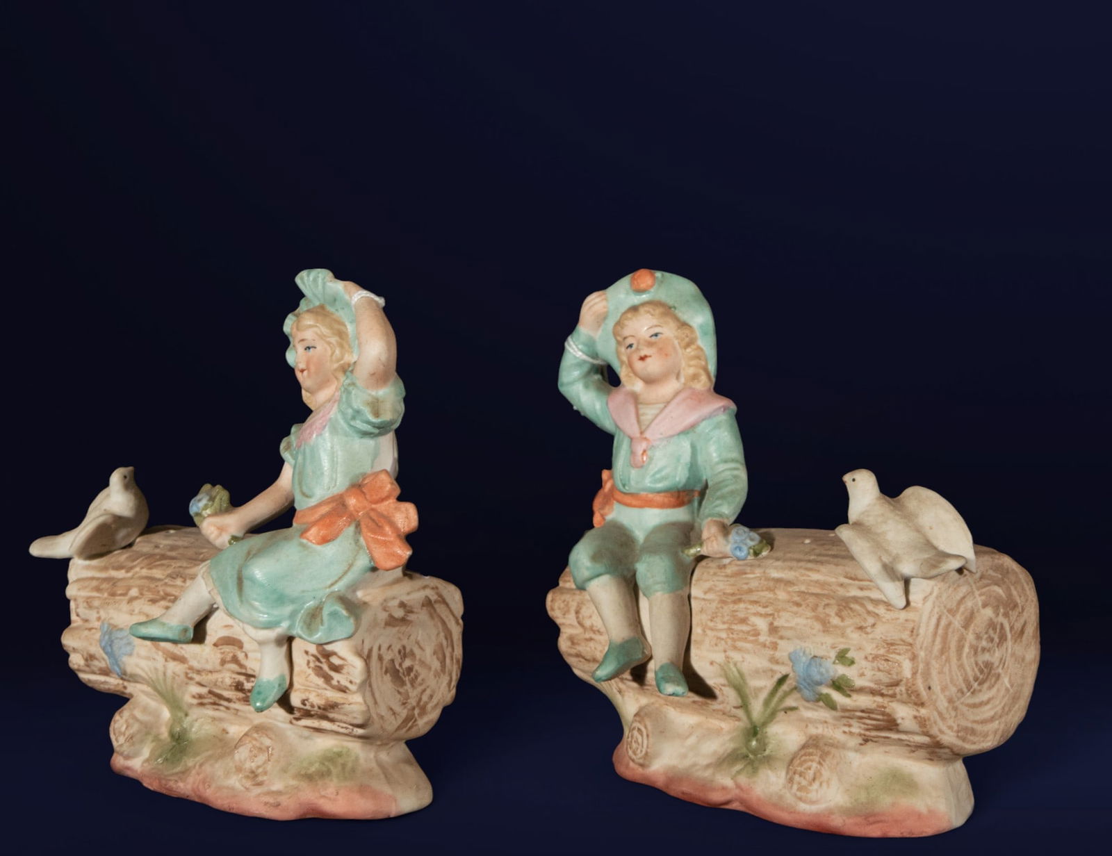 Pair of biscuit toothpick holders with young people. European School. 19th century: Polychrome biscuit. Dimensions: 13 x 13 x 7 cm. A set of two child figures seated on logs, each accompanied by a dove at their feet, evoking bucolic scenes of innocence and candor. The polychromy, in