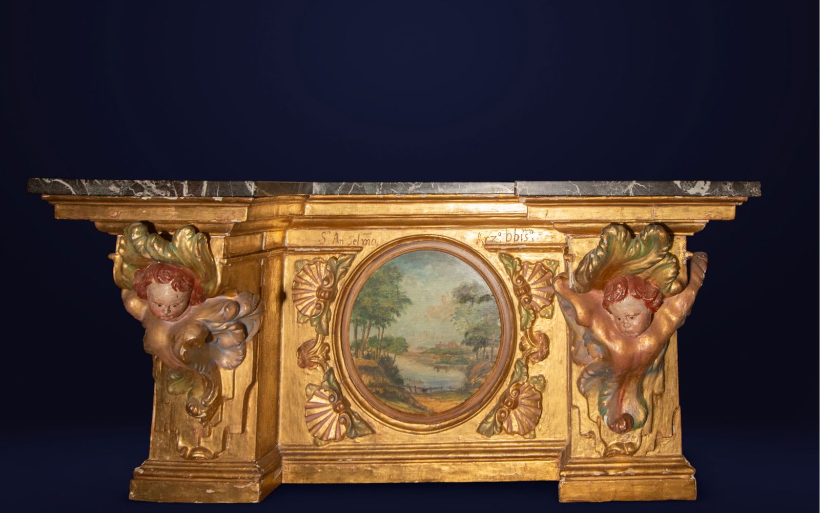 Large Spanish Baroque Sacristy Console, 17th-18th centuries: Carved and gilded wood with a marble top. Dimensions: 83 x 158 x 55 cm. Magnificent Baroque console table with a front decorated with a central landscape framed and flanked by two corbels in the shape