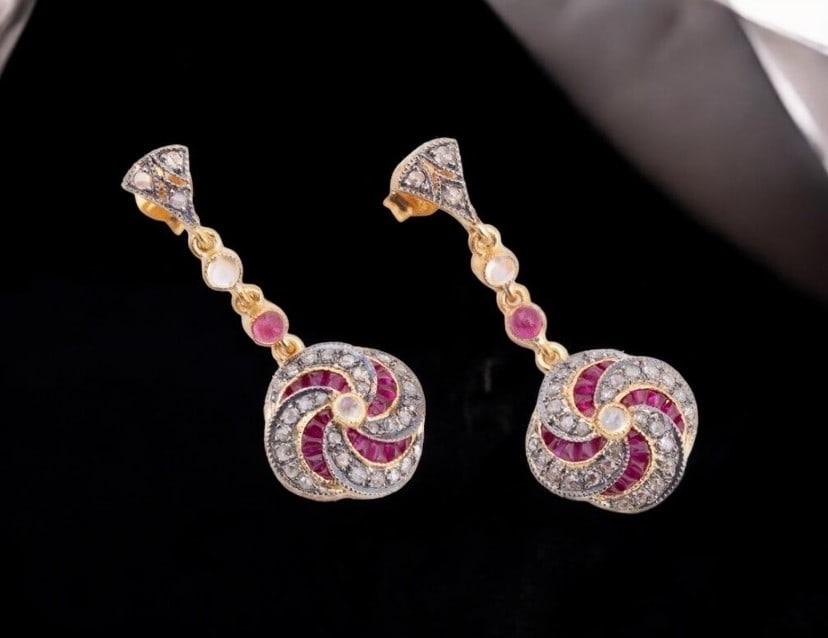 Pair of dangle earrings with rubies, moonstone and diamonds: Pair of drop earrings in 925 sterling silver with gilt plating, featuring 14-karat gold posts and clasps. The ornate design combines rose-cut diamonds with natural rubies and small moonstones. It incl