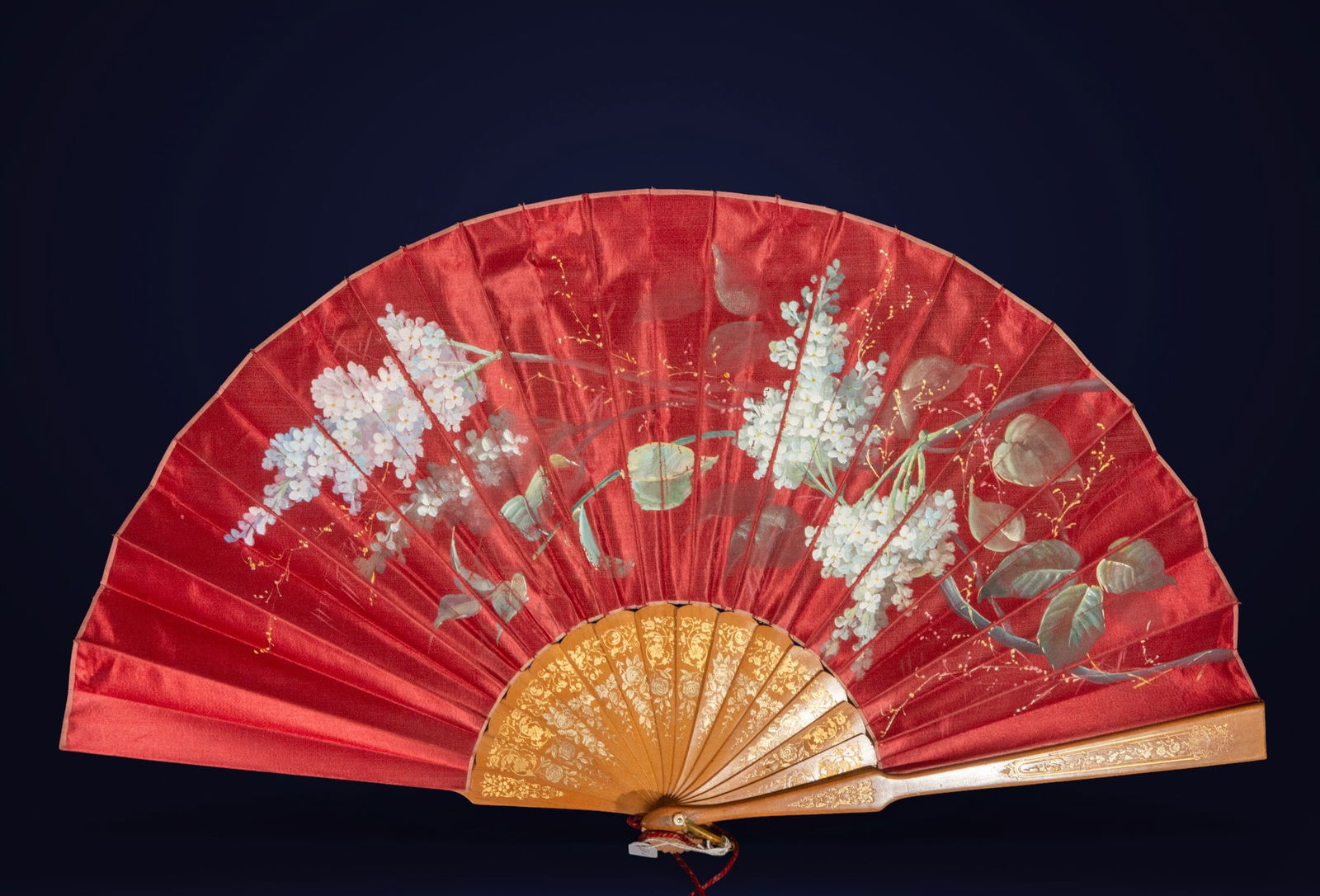 Hand-painted silk fan. Spanish School. 20th century.: Large-format fan with engraved gilt wooden sticks and red silk fabric decorated with hand-painted floral bouquets in lilac, green, and white tones. Measures 35 x 65 x 40 cm. The floral composition, wi