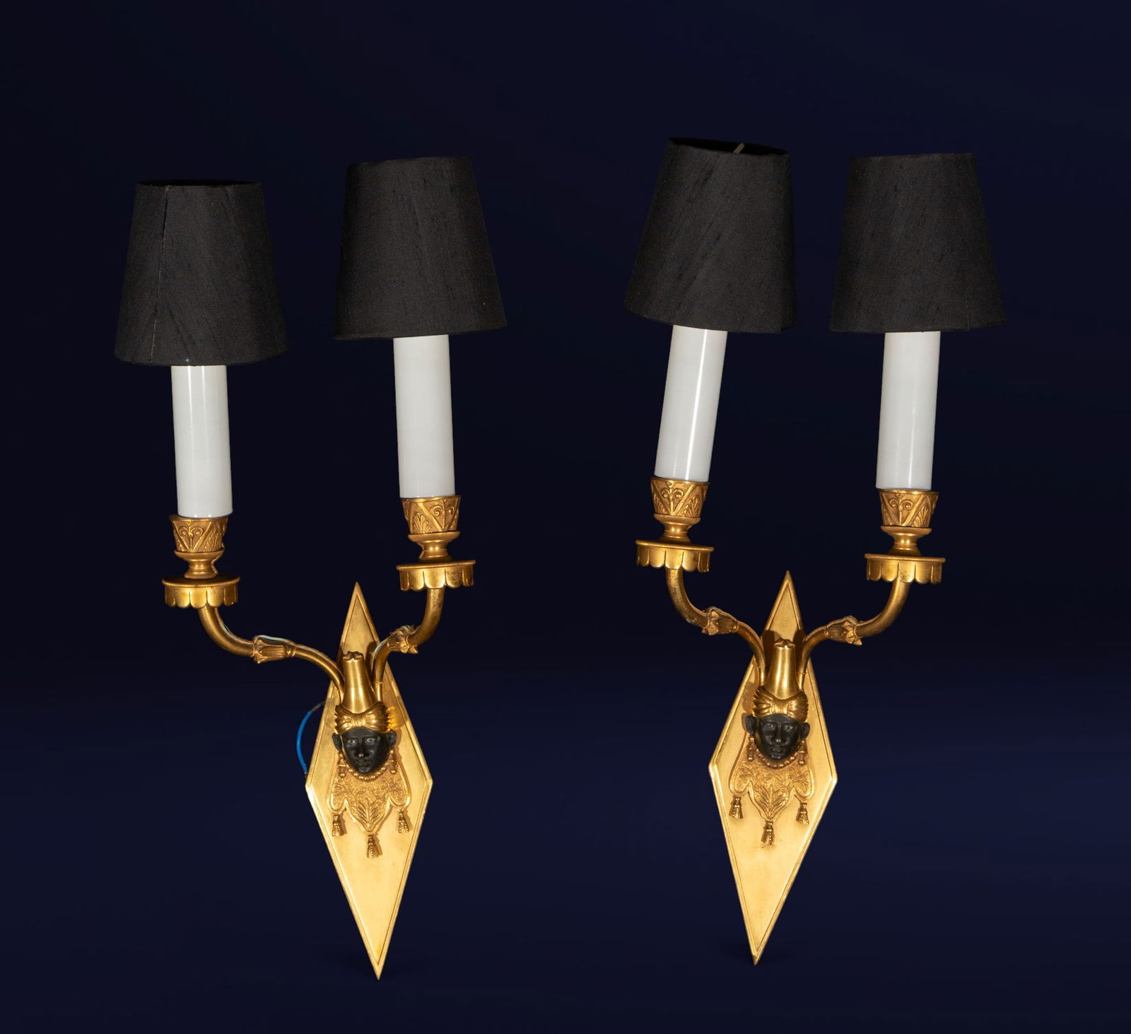 Pair of wall sconces with blackamoor, French School, 19th Century: Gilt and blued bronze. Dimensions: 32 × 19 × 14 cm; 51 cm (with shades). Set of two wall sconces with dark bronze Moorish or "Blackamoor" masks, crowned by bifurcated gilt arms and black fabric shad