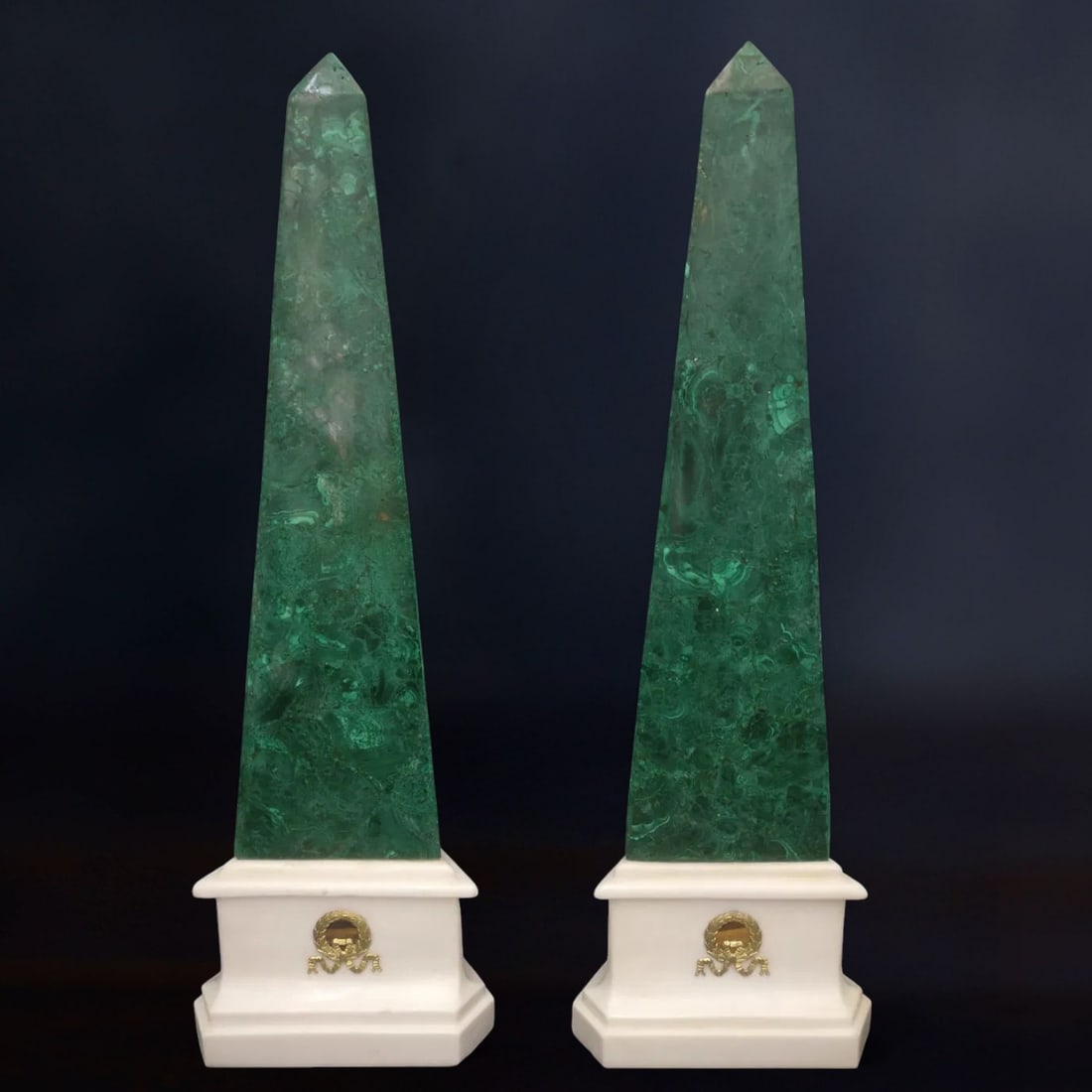 Pair of malachite obelisks with Carrara marble bases and gilt bronze appliqués, Italy, 20th century: Malachite, Carrara marble, and gilt bronze. Dimensions: height 71 cm; base 19 × 19 × 19 cm (each). A set of extraordinary quality and presence, finely crafted, with elegant gilt bronze friezes and M