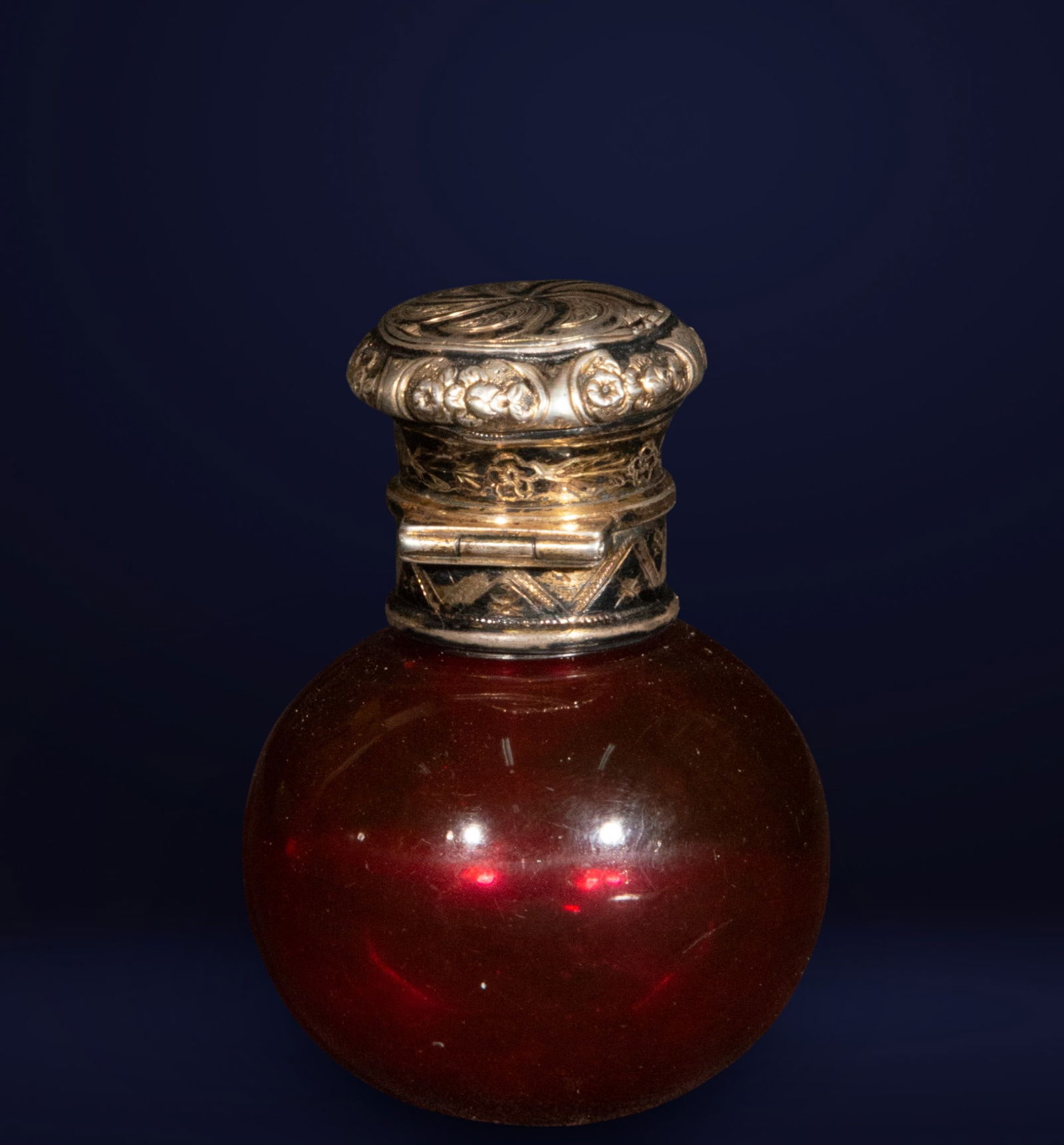 French flask in ruby-colored crystal with a chased silver lid. French school. 19th century.: Small spherical bottle in ruby-colored glass with a hinged lid in embossed silver, decorated with floral and geometric motifs. Dimensions: 6 x 4 x 4 cm. A piece of refined 19th-century taste, typical