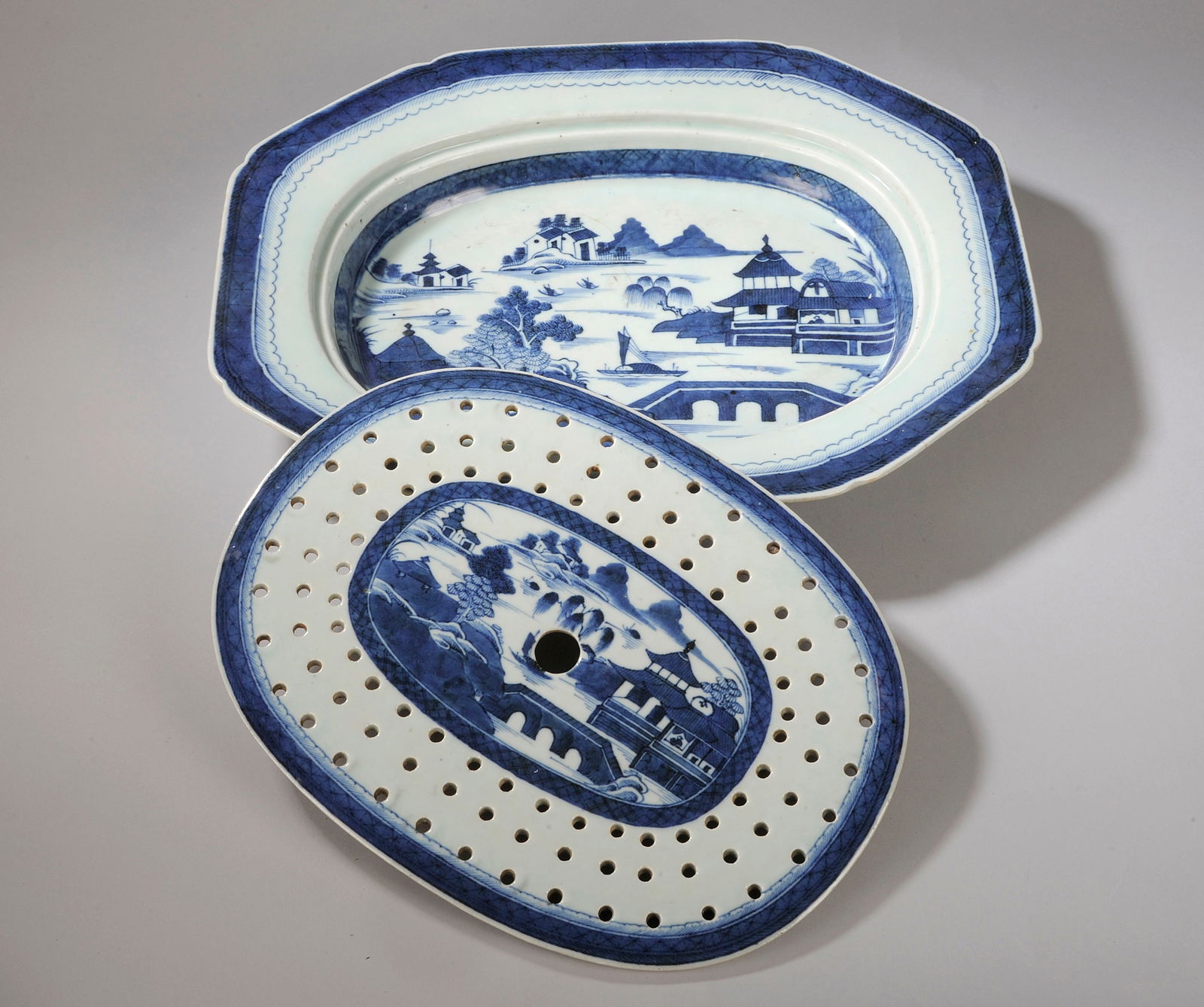 East India Company draining plate, China, 18th century: White porcelain decorated with cobalt blue underglaze. Measures 43.5 x 35 cm. Asparagus draining plate composed of two elements: one openwork and the other a container, both decorated with lakeside la
