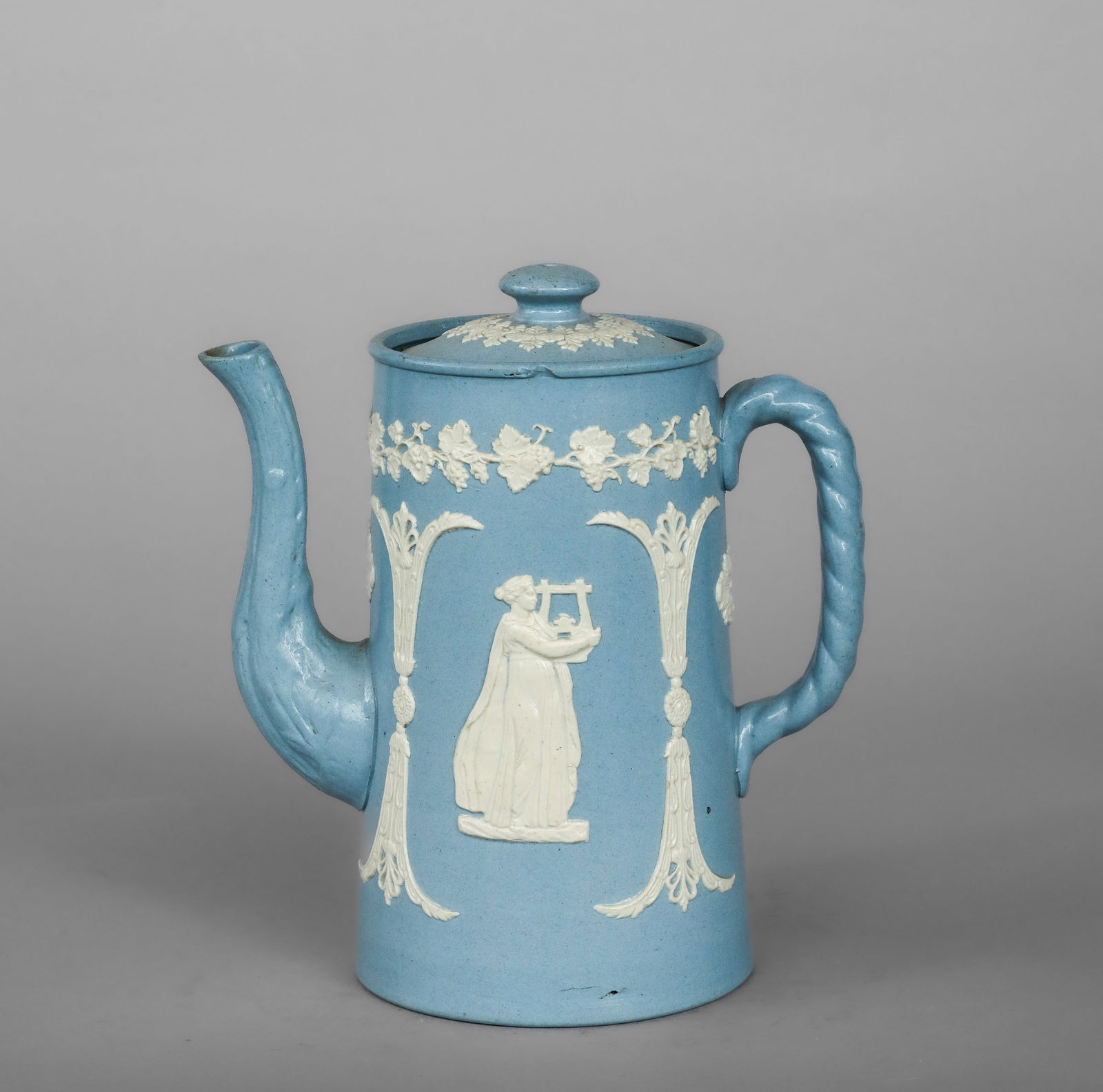 Verseuse with classical female figures in relief, English manufacture, 19th century: Blue powder-glazed ceramic bisque with white relief decoration and a ceramic lid. Measures 20 x 17 cm. This pouring vessel has a cylindrical profile and balanced proportions, featuring a tubular spout