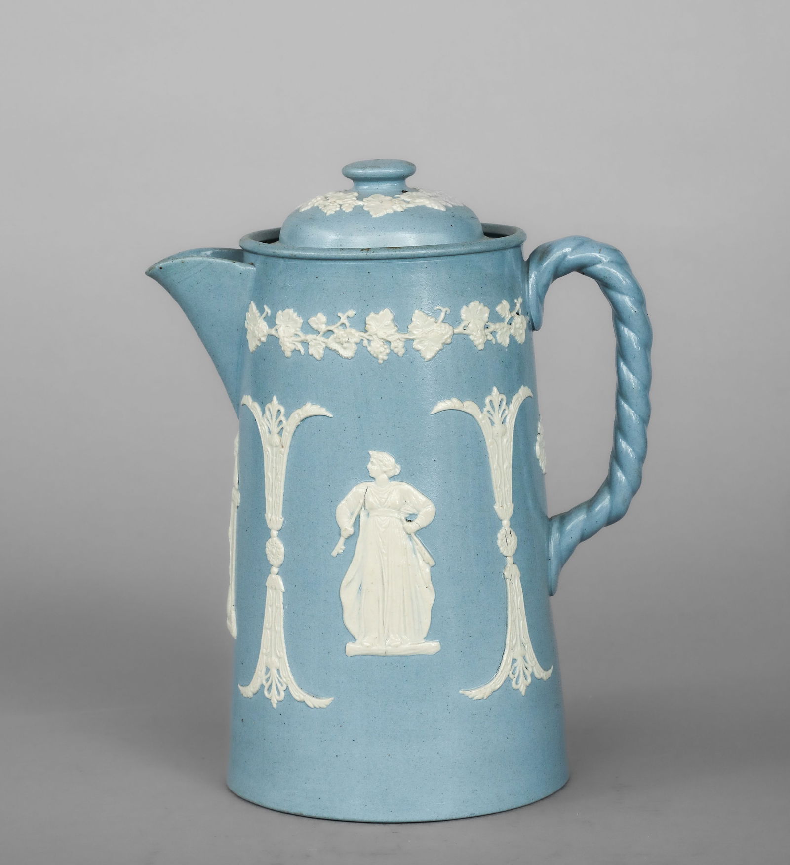 Verseuse with classical female figures in relief, English manufacture, 19th century: Blue powder glazed ceramic bisque with white relief decoration and a ceramic lid. Measures 23 x 10 cm. This cylindrical pourer features clean lines, a tubular spout, and a twisted handle that introduc