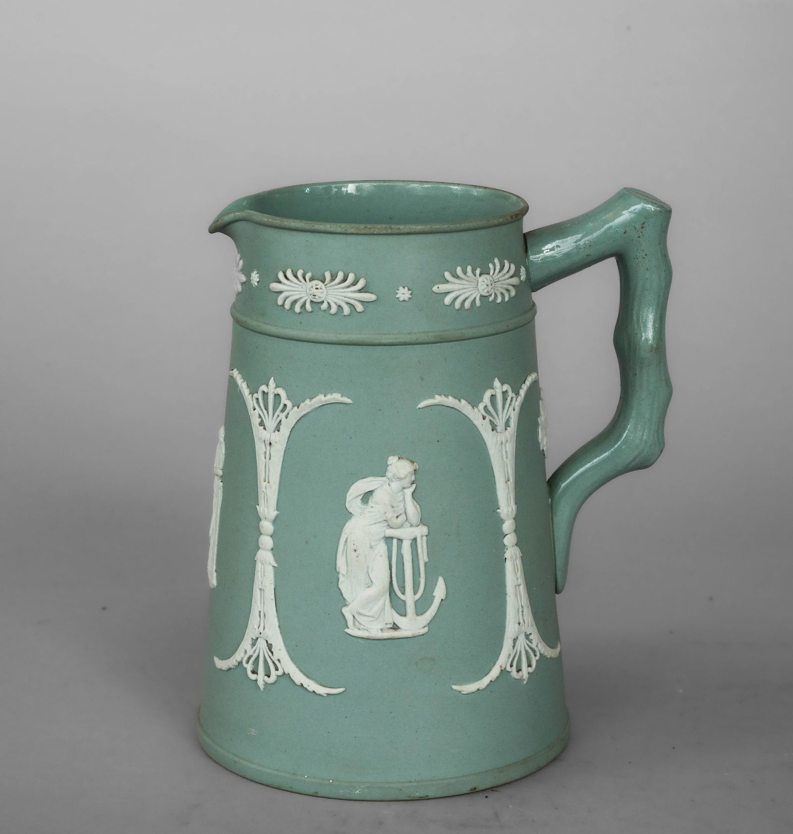 Verseuse with classical female figures in relief, English manufacture, 19th century: Ceramic bisque glazed in greenish celadon gray with white relief decoration. Measures 16 x 8 cm. Small-format pourer with a gently flared cylindrical body, integrated spout, and a handle modeled in th