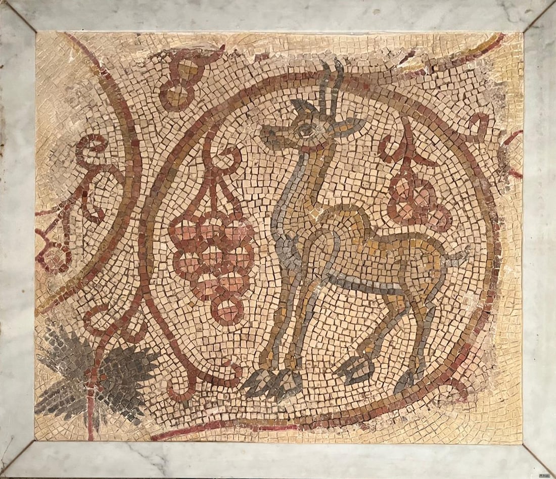 Antique mosaic panel with deer and vine decoration, Late Roman or Early Christian period, 4th - 6th: Polychrome natural stone tesserae. Decorative fragment organized around a central circular medallion depicting a stylized deer, rendered in ochre, brown, and gray tones, its elegant silhouette set aga