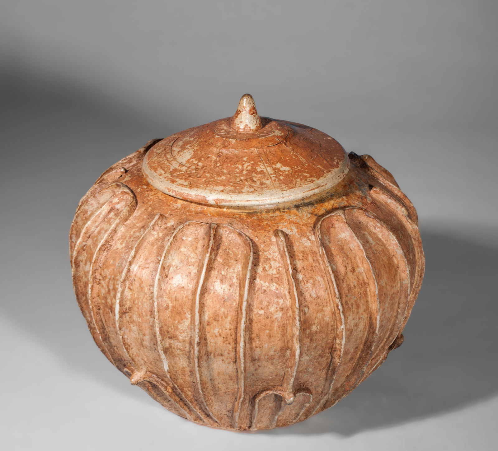 Globular pot with fluted lid and lotus petals, China, Jin Dynasty, 3rd-5th century: Terracotta. Globular vessel with a lid, entirely modeled in broad vertical ridges reminiscent of lotus petals, a symbolic motif associated with purity and rebirth. The surface has a matte, slightly ir