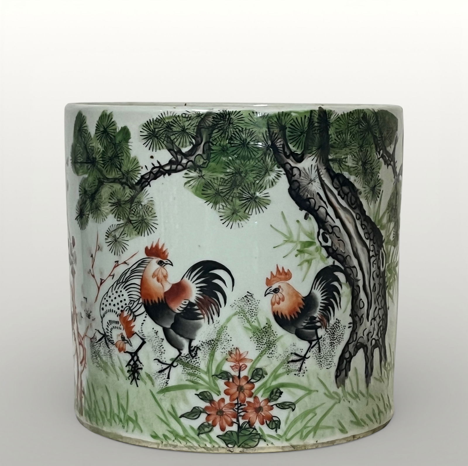 Bitong with roosters and landscape, Chinese porcelain, 20th century: Pink-colored glazed porcelain. Dimensions not specified. Cylindrical brush holder decorated with a continuous scene depicting three roosters with black, white, and brown plumage in a natural setting o