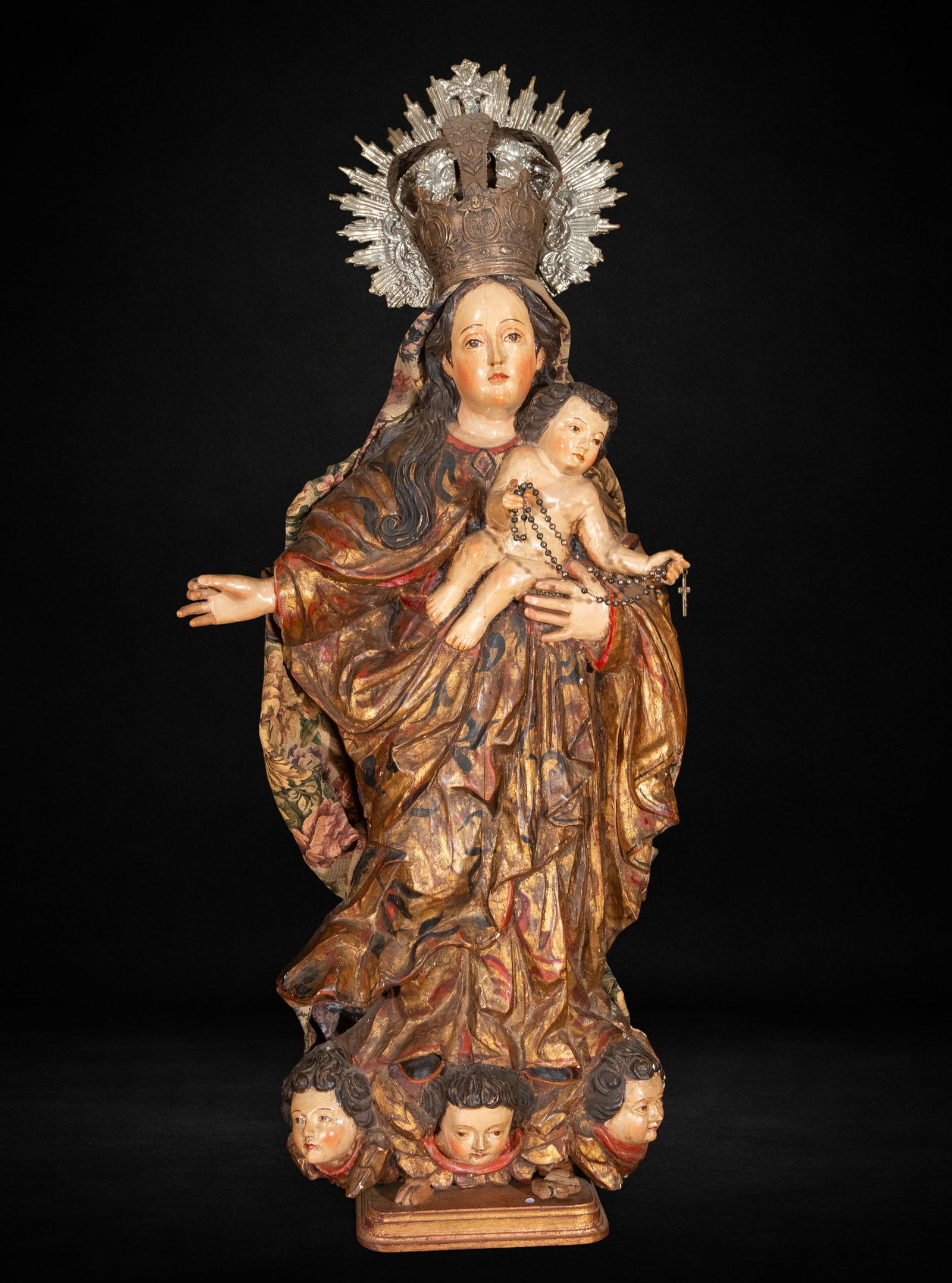 Baroque Virgin and Child with Peruvian silver crown. 18th-19th century: Polychrome wood carving. Measures 105 x 56 x 21 cm. The Virgin holds the Child on her left arm, while her right arm is outstretched in a gesture of offering. The composition displays a marked frontali