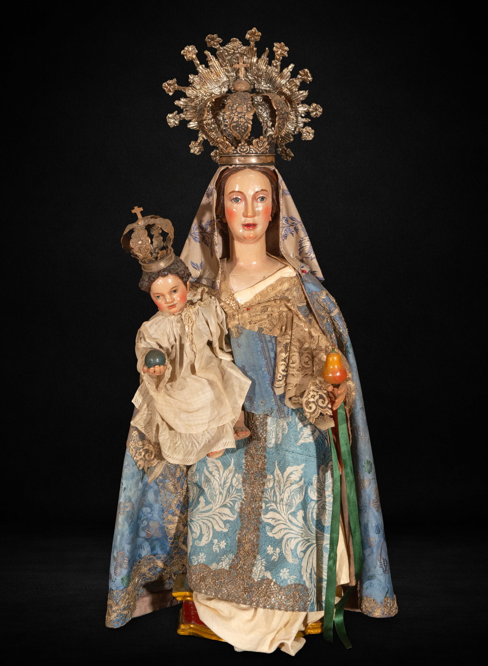 Virgin and Child dressed in a silver crown. 17th century: Polychrome wood carving for dressing. Measures 101 x 40 x 27 cm. The Virgin holds the Child in a frontal pose, creating a balanced and solemn composition. The Child carries a symbolic sphere while the