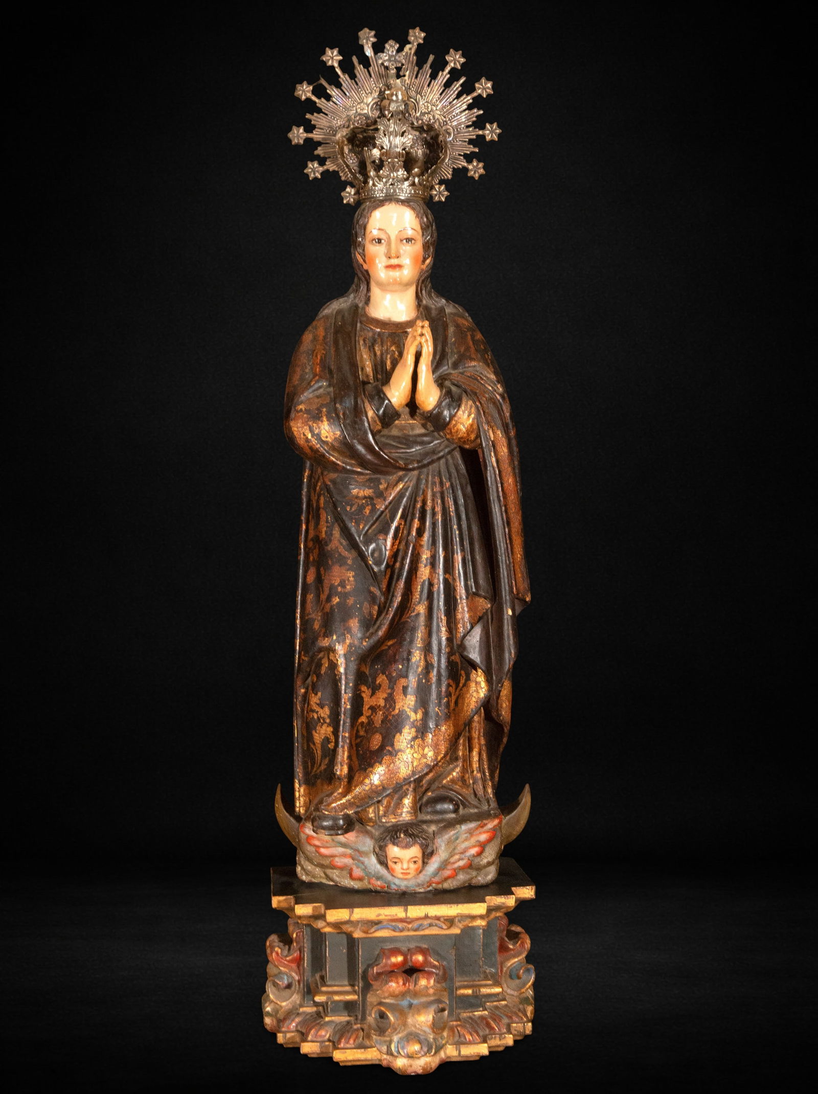 Important Immaculate Virgin, Primitive Colonial Mexico, 17th Century: Carved and polychromed wood. Virgin measures 115 x 36 x 26 cm; total 140 x 38 x 26 cm. Image of the Immaculate Virgin in a praying posture, with hands joined on her chest, crowned and positioned on a