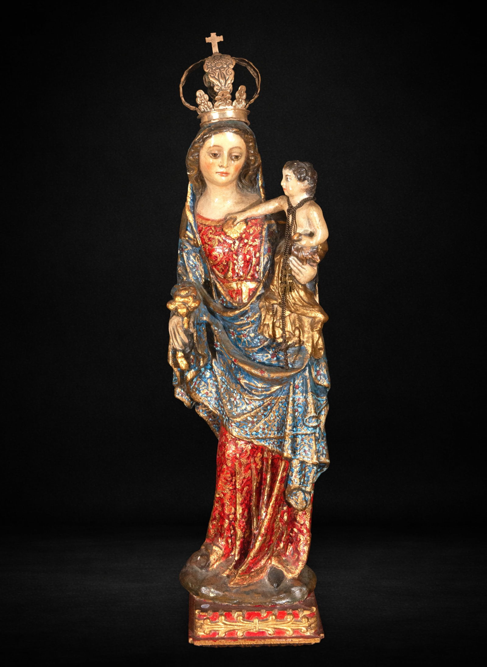 Virgin and Child in plaster, first half of the 20th century: Polychrome plaster. Measures 71 x 20 x 15 cm. Image of the crowned Virgin holding the Child in her left arm, with a mantle decorated in shades of blue and gold and a reddish tunic with ornamental moti