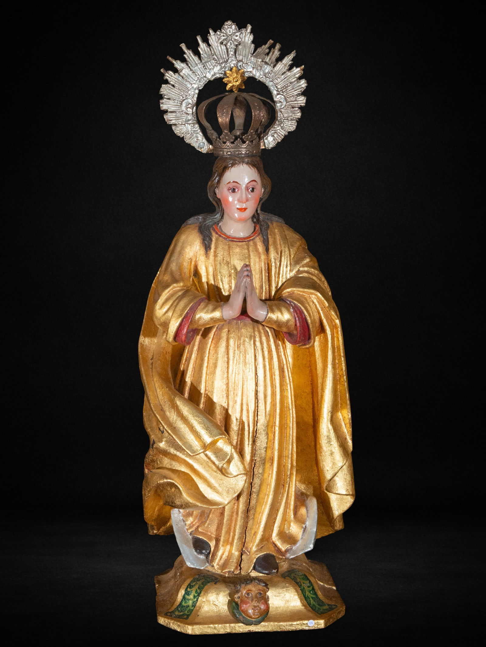 Immaculate Virgin, Colonial School, 17th Century: Carved, polychromed and gilded wood. Standing Virgin with hands in prayer, richly gilded garments and metal crown, resting on a crescent moon and cherub's head; composition of marked verticality and g