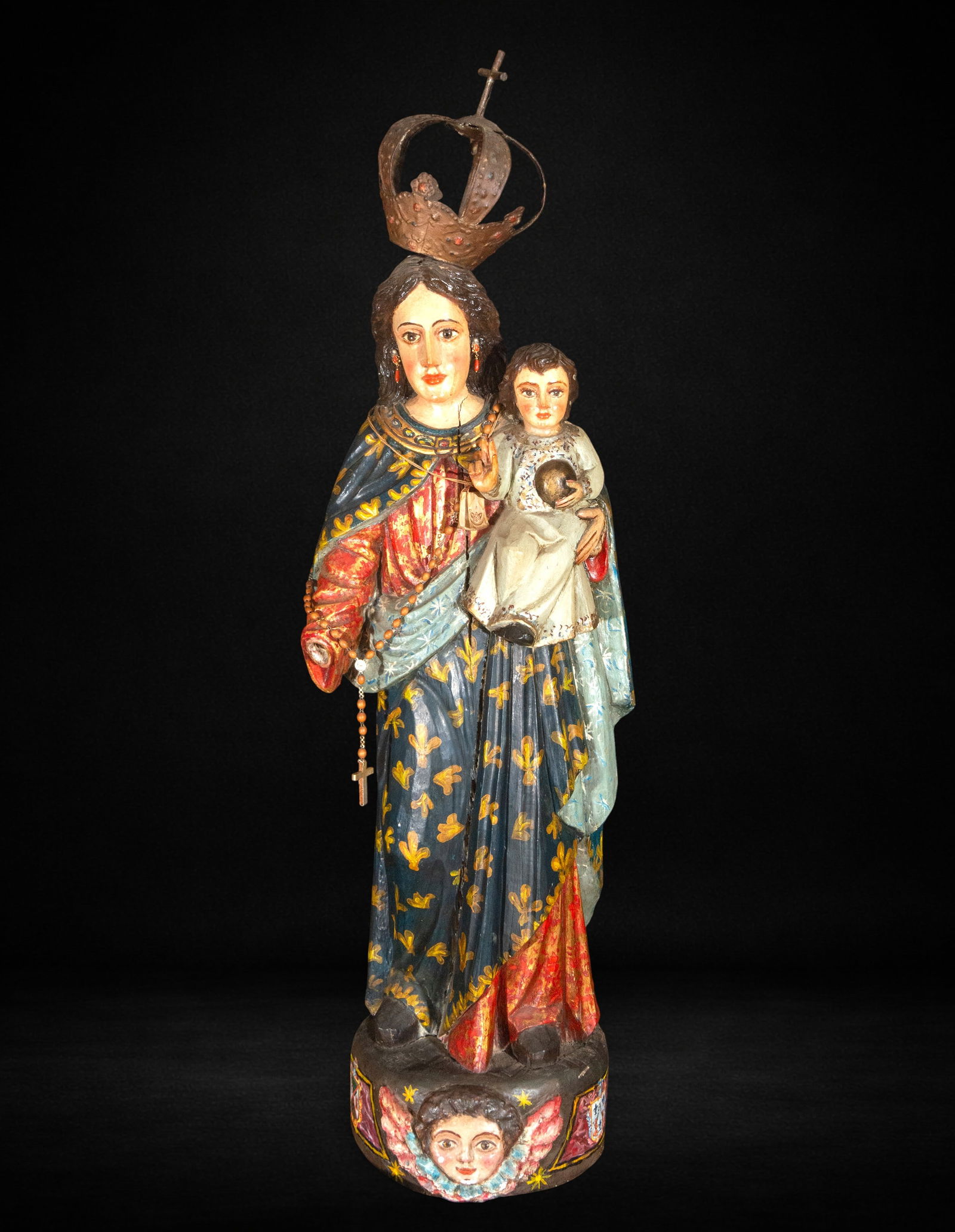 Our Lady of the Rosary, colonial school, 18th century: Carved and polychromed wood. Measures 100 x 35 x 22 cm. Image of the Virgin with the Child in her left arm and a rosary hanging in her right hand, crowned and dressed in ample robes decorated with gol