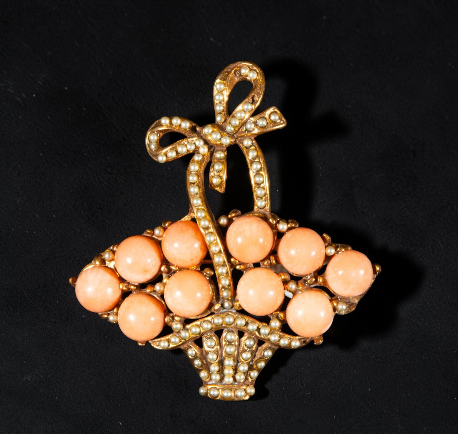 Brooch in gilded silver and coral: A brooch in gilded silver and coral. Designed in the shape of a basket topped with a bow, it features several spherical coral beads in a uniform pink hue set on a gold-plated frame adorned with small,