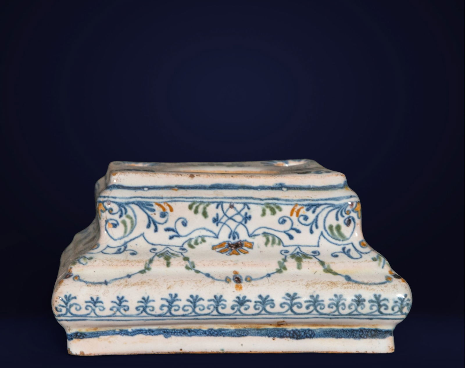French Moustiers Ceramic Inkwell - 19th Century: Glazed and painted ceramic. Dimensions: 6 × 10 × 10 cm. Small pedestal or base with a molded profile and linear and vegetal decoration in blue, green, and yellow on a white background. Its design co