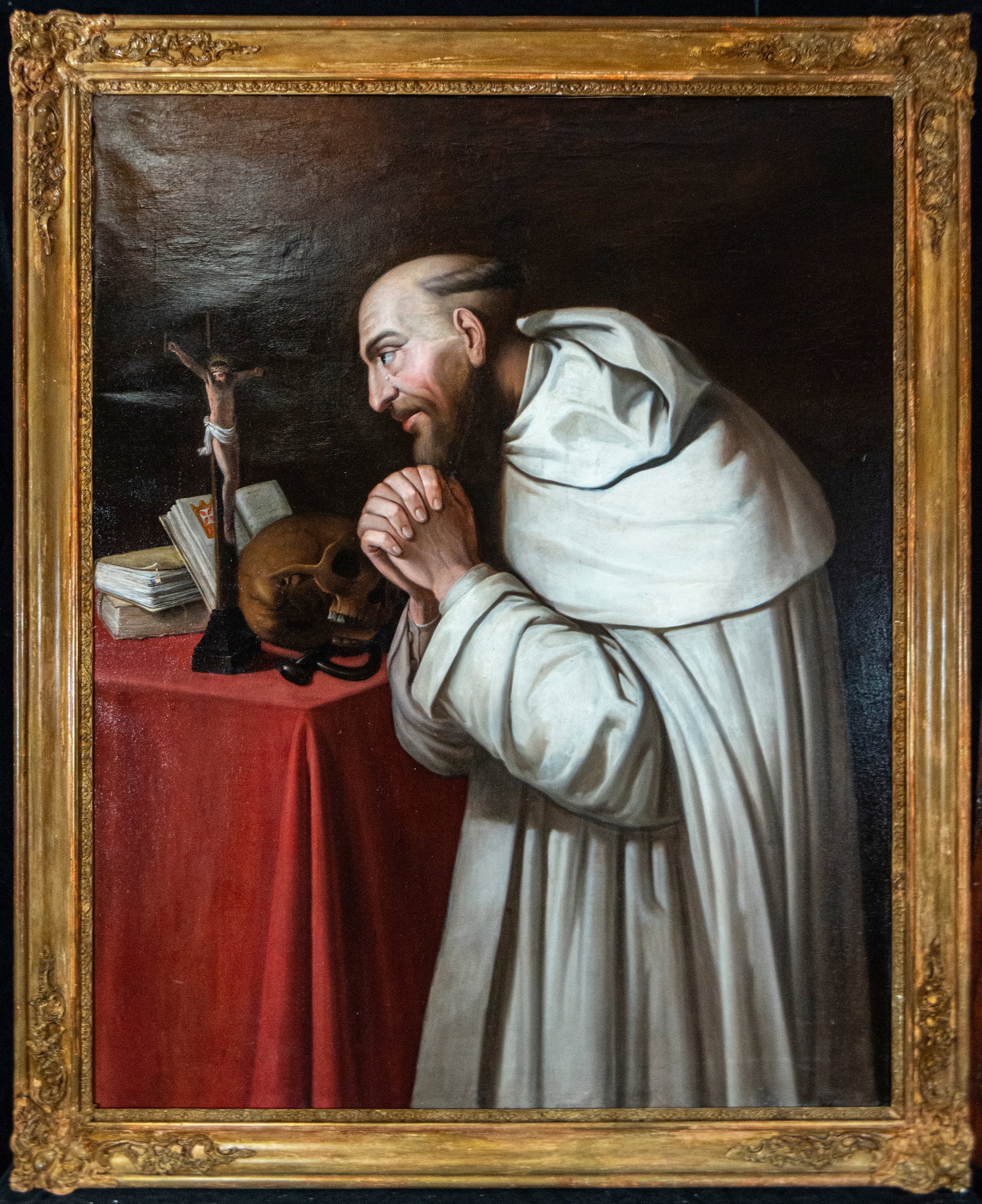 Saint of the Order of Jerusalem in prayer, Italian, 18th century: Oil on canvas. Dimensions 144 x 90 / 130 x 107 cm. Devotional image of a Carthusian monk bent in deep contemplation before a table covered with a red cloth, upon which rest a crucifix, books, a skull,