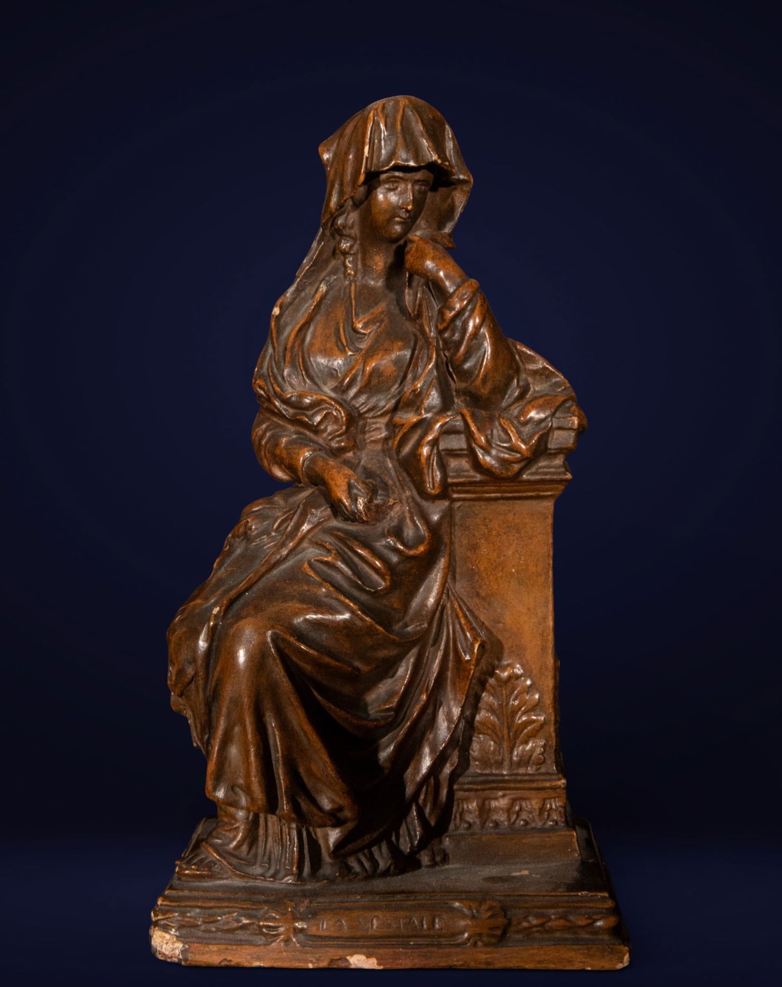 Vestal seated. Art nouveau. 19th century: Patinated terracotta. Measures 26 x 14 x 10 cm. A seated female figure with an elegant, Symbolist air, covered with a veil and flowing drapery, leans thoughtfully against a classically inspired archit