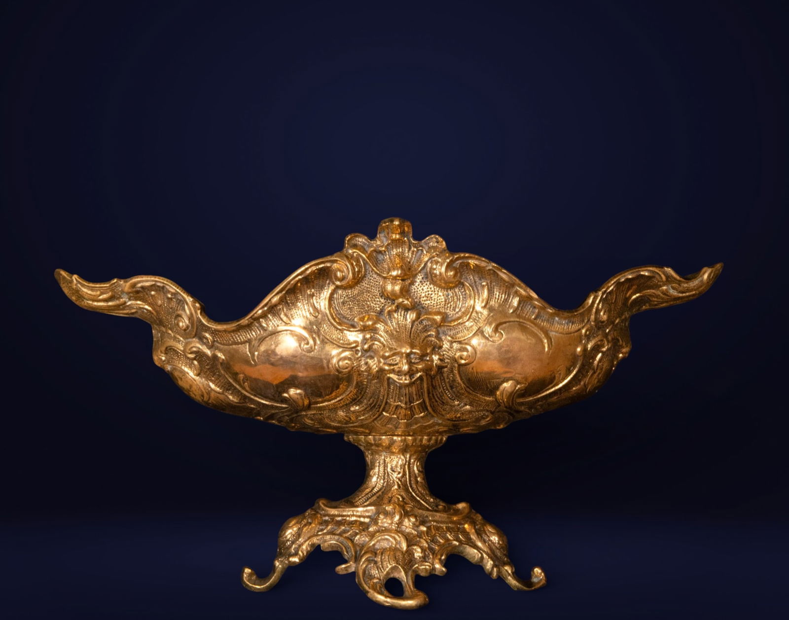 Gilded bronze centerpiece, Rococo style, 20th century: Gilded and cast bronze. Measures 23 x 44 x 25 cm. This centerpiece features an elongated, sinuous profile, with an open, boat-shaped body and elegantly flared ends, articulated by profuse decoration o